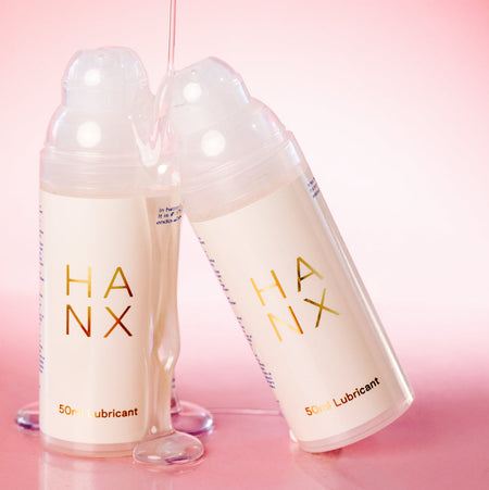 A 50ml bottle of HANX vegan lubricant leaning against another bottle, with a smooth clear liquid dripping between them.