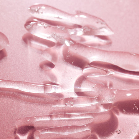 Close-up of the HANX lubricant liquid, clear and smooth on a pink background.